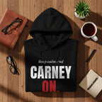 Black hoodie with "CARNEY ON." text, on a wooden surface with desk accessories.