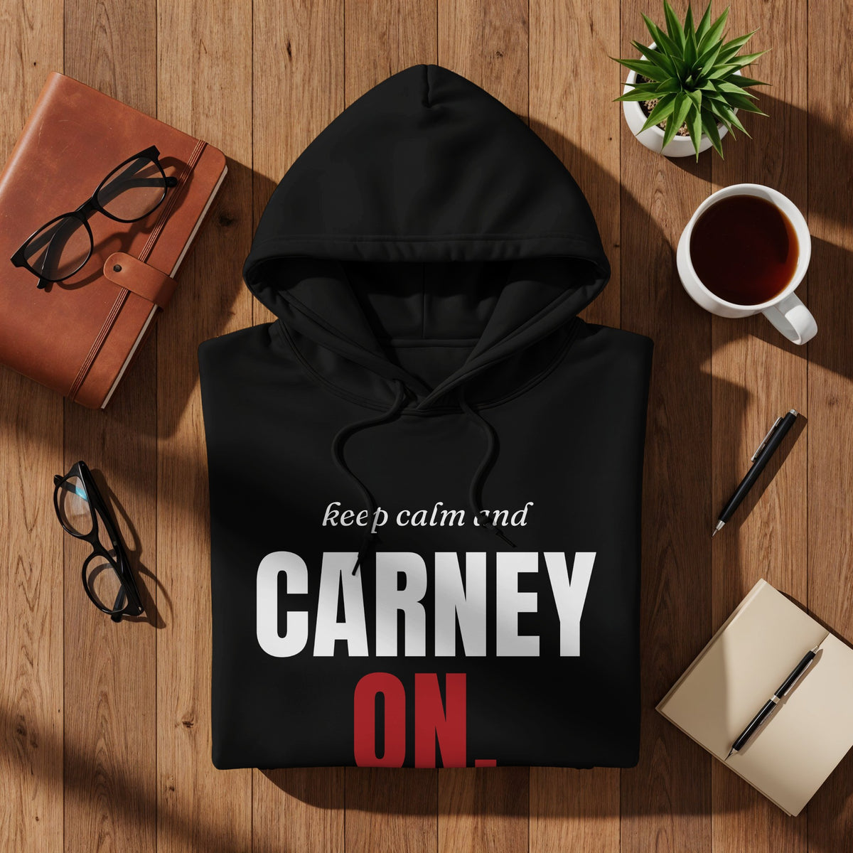Black hoodie with "CARNEY ON." text, on a wooden surface with desk accessories.