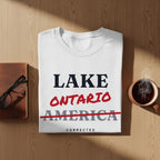 White t-shirt with text "LAKE ONTARIO" in red, and "AMERICA" crossed out in red, with "CORRECTED" below.