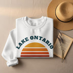 White sweatshirt with "Lake Ontario" text and a retro sunset graphic.